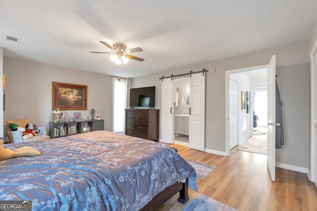 bedroom featuring a barn door, visible vents, baseboards, light wood finished floors, and ensuite bath