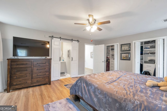 bedroom featuring multiple closets, visible vents, ensuite bathroom, a barn door, and wood finished floors