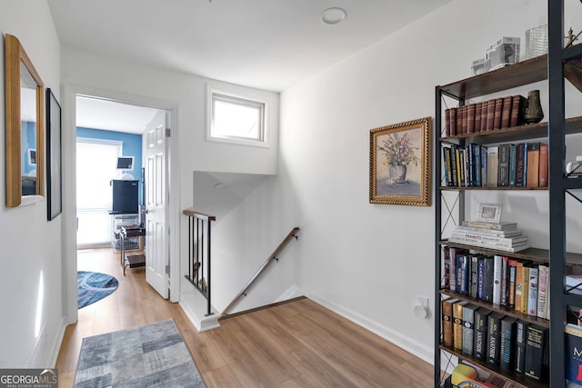 corridor featuring baseboards, an upstairs landing, and wood finished floors