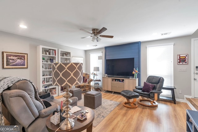 living room featuring light wood-type flooring, baseboards, visible vents, and a ceiling fan