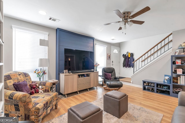 living area with light wood-style floors, ceiling fan, stairs, and visible vents