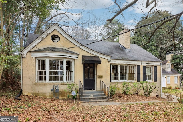 view of front of house with a shingled roof, entry steps, brick siding, and a chimney