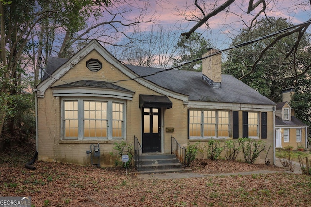 bungalow-style house featuring a shingled roof, brick siding, and a chimney