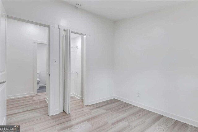 unfurnished bedroom with baseboards, light wood finished floors, a closet, a walk in closet, and connected bathroom