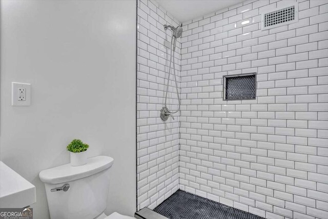 full bath with visible vents, toilet, and tiled shower