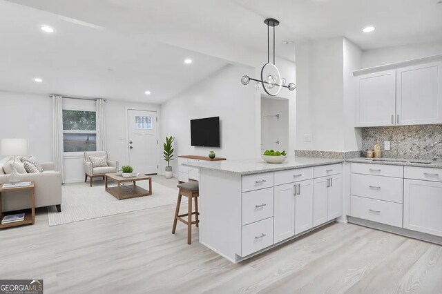 kitchen featuring backsplash, open floor plan, vaulted ceiling, a peninsula, and white cabinetry