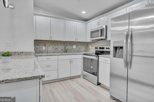 kitchen with a sink, backsplash, appliances with stainless steel finishes, and white cabinetry