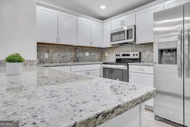 kitchen with white cabinets, light stone countertops, tasteful backsplash, and appliances with stainless steel finishes