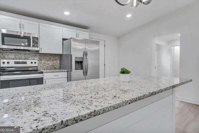 kitchen featuring light stone counters, appliances with stainless steel finishes, white cabinets, and light wood finished floors