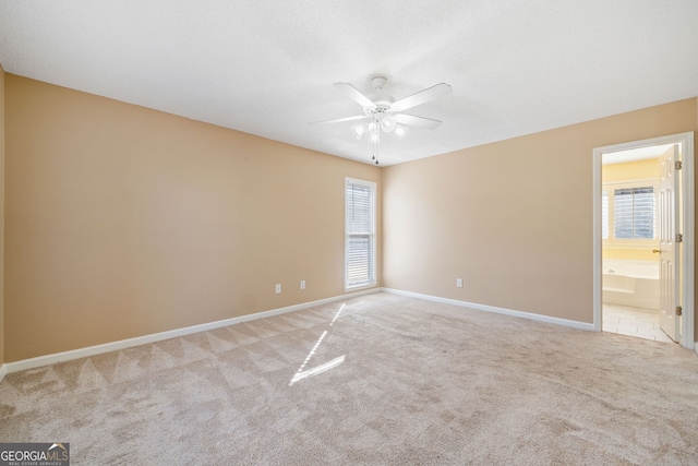 spare room featuring light colored carpet, ceiling fan, and baseboards