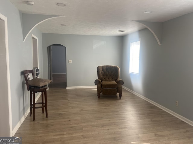 living area with baseboards, a textured ceiling, arched walkways, and wood finished floors