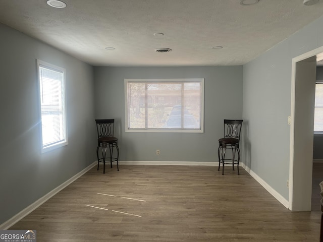 unfurnished room featuring visible vents, a textured ceiling, baseboards, and wood finished floors