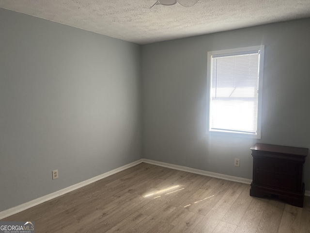 spare room featuring a textured ceiling, baseboards, and wood finished floors