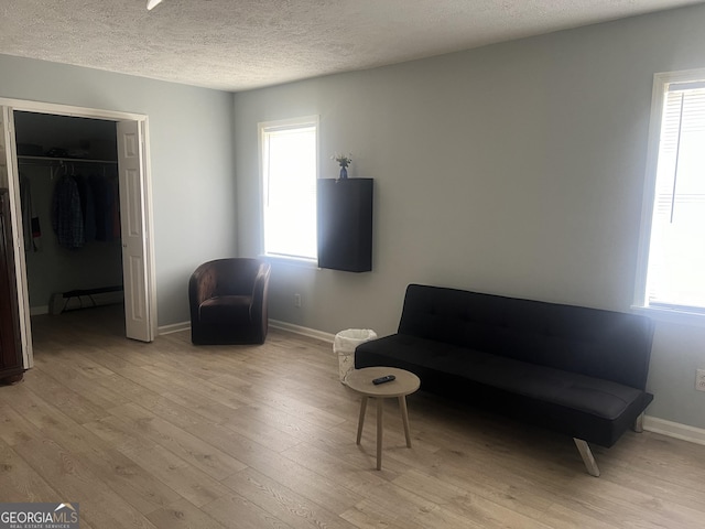 living area with a textured ceiling, light wood-style floors, a baseboard radiator, and a healthy amount of sunlight