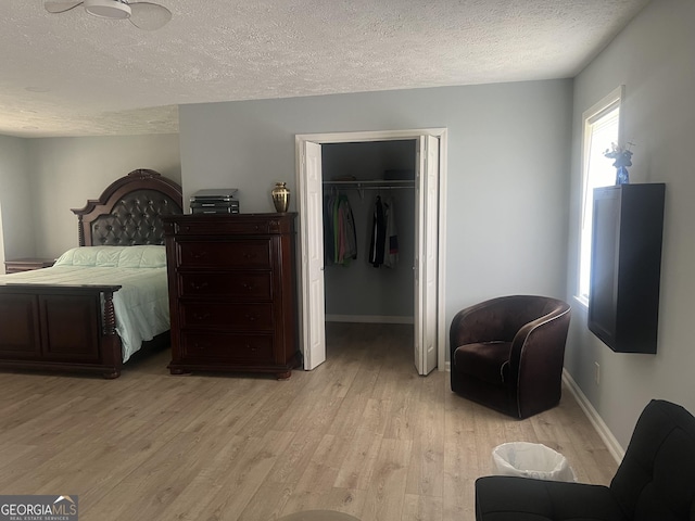 bedroom featuring a textured ceiling, baseboards, light wood-style floors, a spacious closet, and a closet