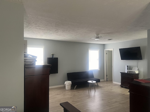 living area with light wood finished floors, ceiling fan, baseboards, and a textured ceiling