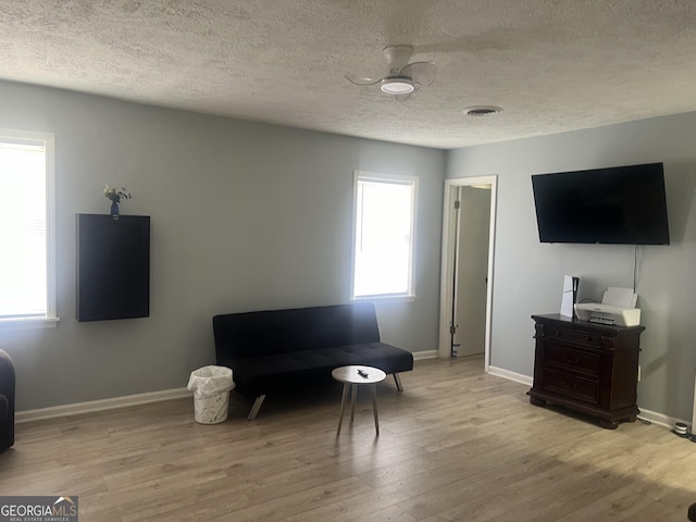 living area featuring a textured ceiling, wood finished floors, visible vents, and baseboards