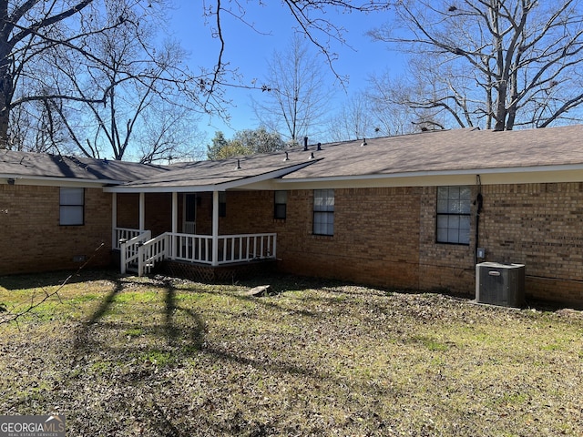 rear view of property with covered porch, a lawn, central AC, and brick siding