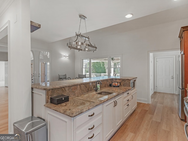 kitchen with light wood finished floors, light stone counters, white cabinetry, pendant lighting, and a sink