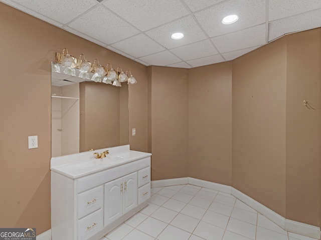 full bathroom featuring a paneled ceiling, baseboards, walk in shower, and vanity