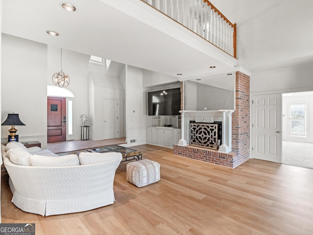 living area with visible vents, a towering ceiling, wood finished floors, a brick fireplace, and recessed lighting