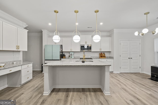 kitchen featuring a sink, white cabinets, freestanding refrigerator, stainless steel microwave, and crown molding