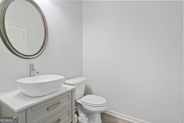 bathroom with toilet, wood finished floors, vanity, and baseboards