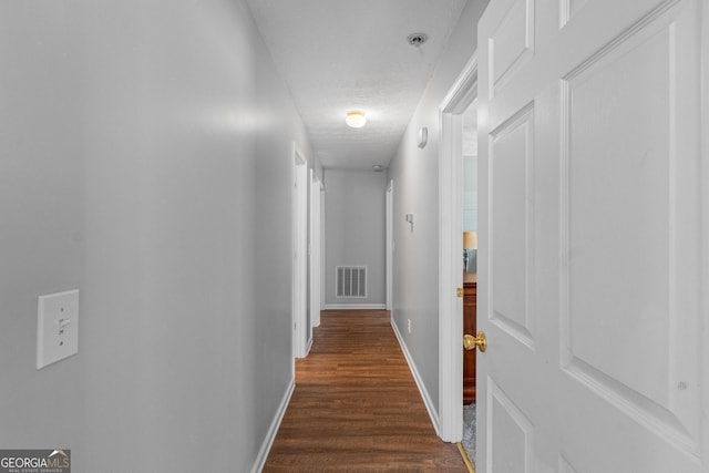 hall featuring baseboards, visible vents, dark wood-style flooring, and a textured ceiling