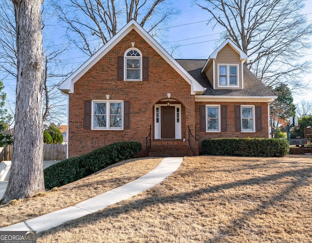 view of front of house with brick siding, roof with shingles, a front yard, and fence