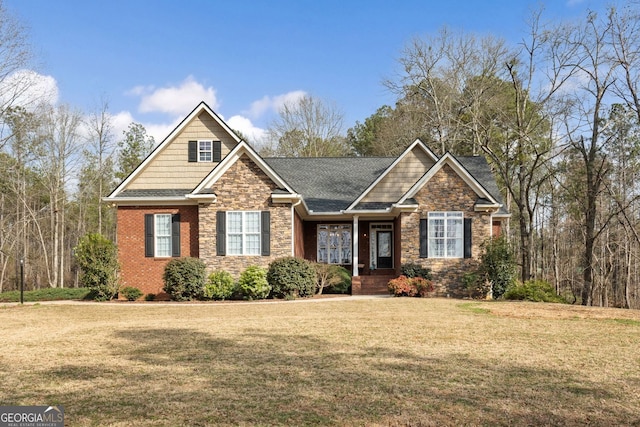 craftsman inspired home featuring stone siding, a shingled roof, a front lawn, and brick siding