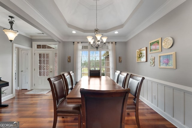 dining area with dark wood-style floors, a tray ceiling, ornamental molding, and an inviting chandelier