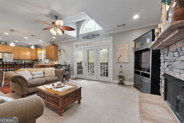 living area featuring visible vents, baseboards, a ceiling fan, crown molding, and a stone fireplace