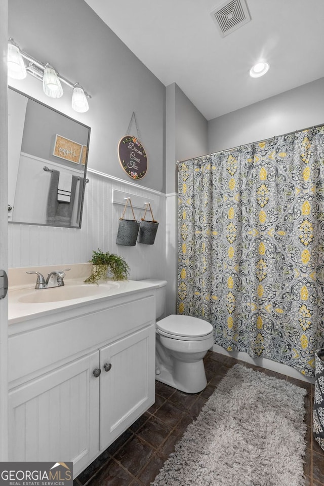 bathroom with a wainscoted wall, curtained shower, visible vents, toilet, and vanity