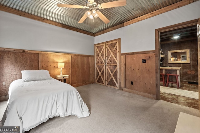 carpeted bedroom with a ceiling fan, a wainscoted wall, and wood walls