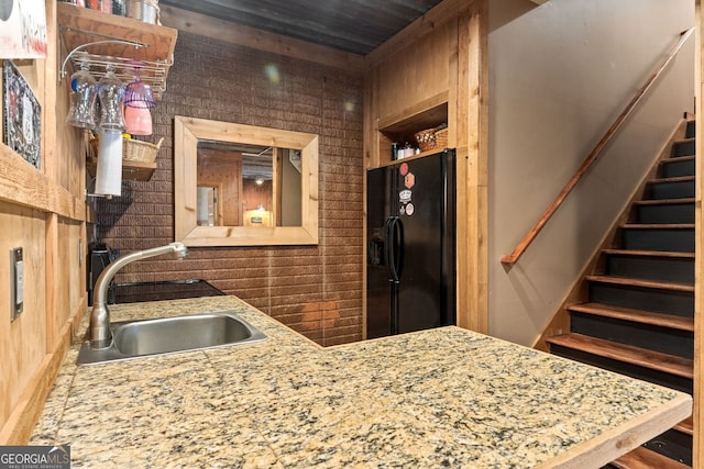 kitchen with wood walls, a sink, open shelves, and black fridge