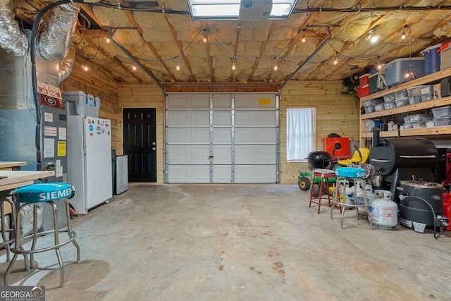 garage with a garage door opener, freestanding refrigerator, and wood walls