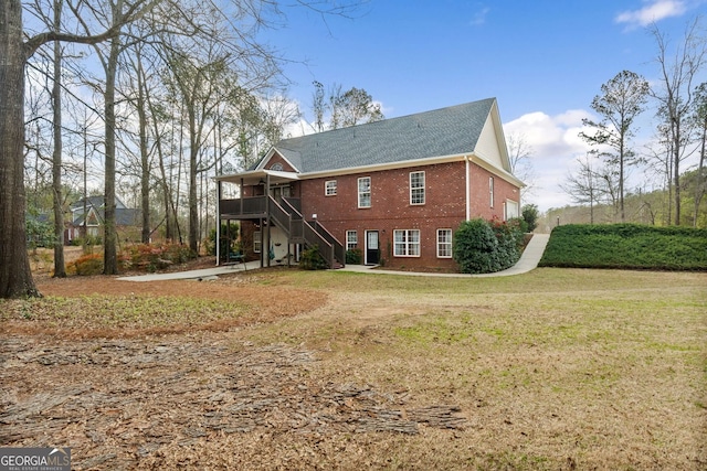 rear view of property featuring a wooden deck, stairway, a lawn, and brick siding