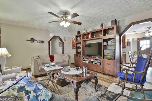 living room with ceiling fan, a textured ceiling, and light wood finished floors