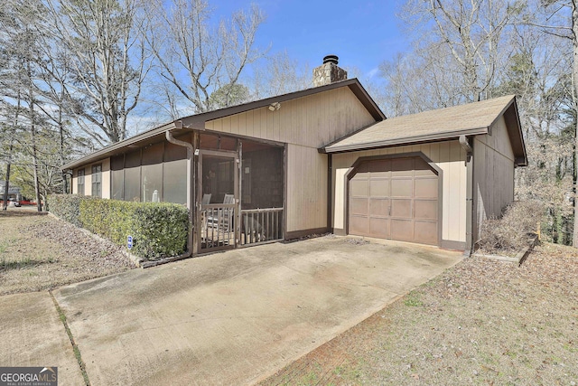 view of home's exterior featuring a garage, a sunroom, a chimney, and concrete driveway