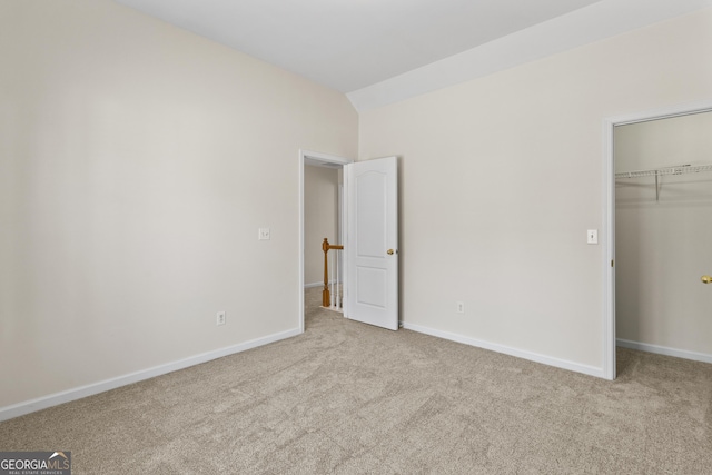 unfurnished bedroom with carpet floors, a walk in closet, a closet, vaulted ceiling, and baseboards