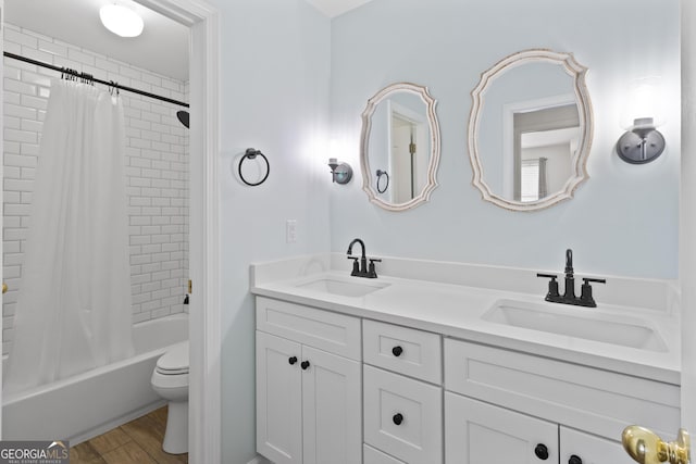 bathroom with toilet, double vanity, a sink, and wood finished floors