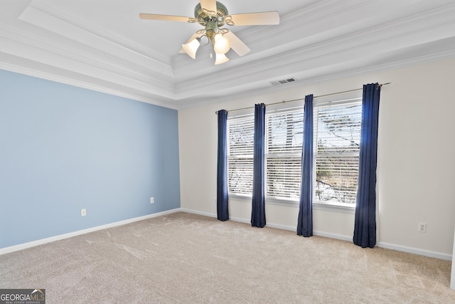 carpeted empty room with crown molding, a raised ceiling, visible vents, a ceiling fan, and baseboards