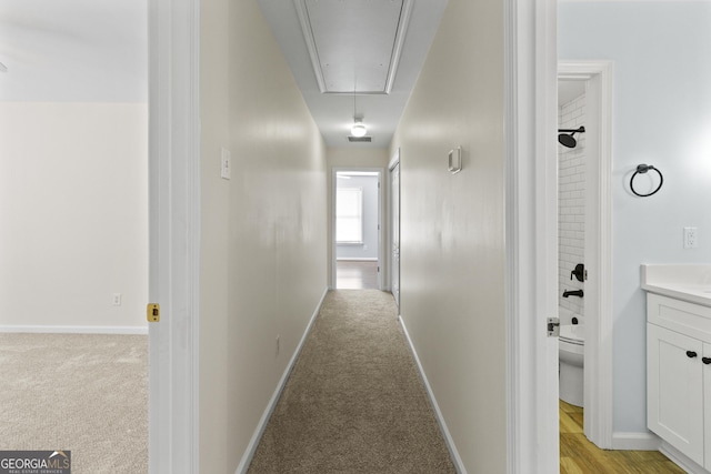 hall with baseboards, attic access, and light colored carpet