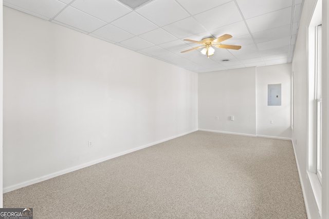 carpeted spare room with a ceiling fan, baseboards, electric panel, and a drop ceiling