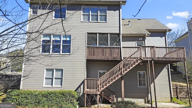 rear view of property featuring a shingled roof, stairway, a wooden deck, and a sunroom