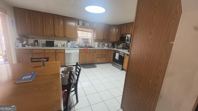 kitchen featuring light tile patterned flooring, a sink, light countertops, appliances with stainless steel finishes, and brown cabinetry