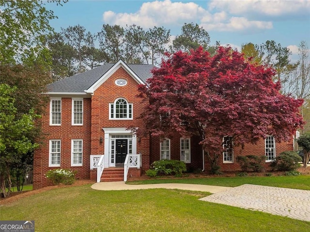 view of front facade with a shingled roof, a front yard, and brick siding