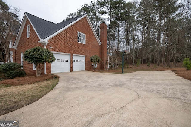 view of side of property with a garage, a shingled roof, concrete driveway, a chimney, and brick siding