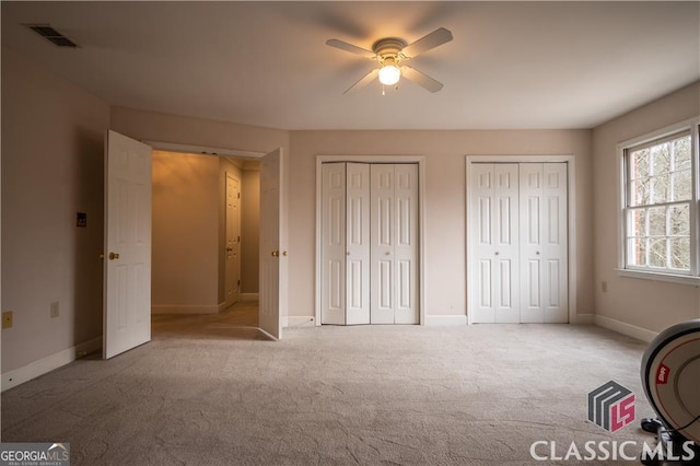 unfurnished bedroom featuring ceiling fan, visible vents, baseboards, carpet, and two closets