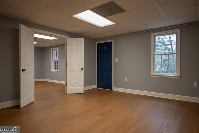 basement featuring light wood-type flooring, baseboards, and a drop ceiling